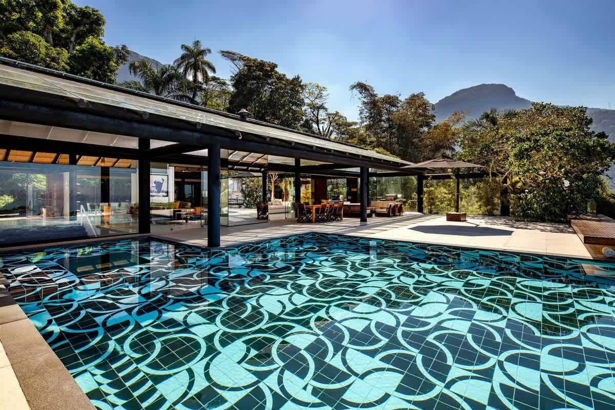 The villa from the pool deck — glass pavilion, mosaic pool, mountain behind.