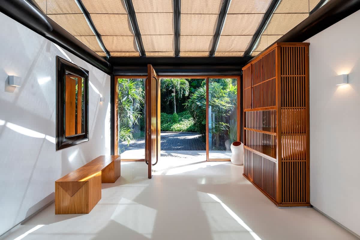 Entrance foyer with wood pivot door, slatted screen, and woven shade canopy.