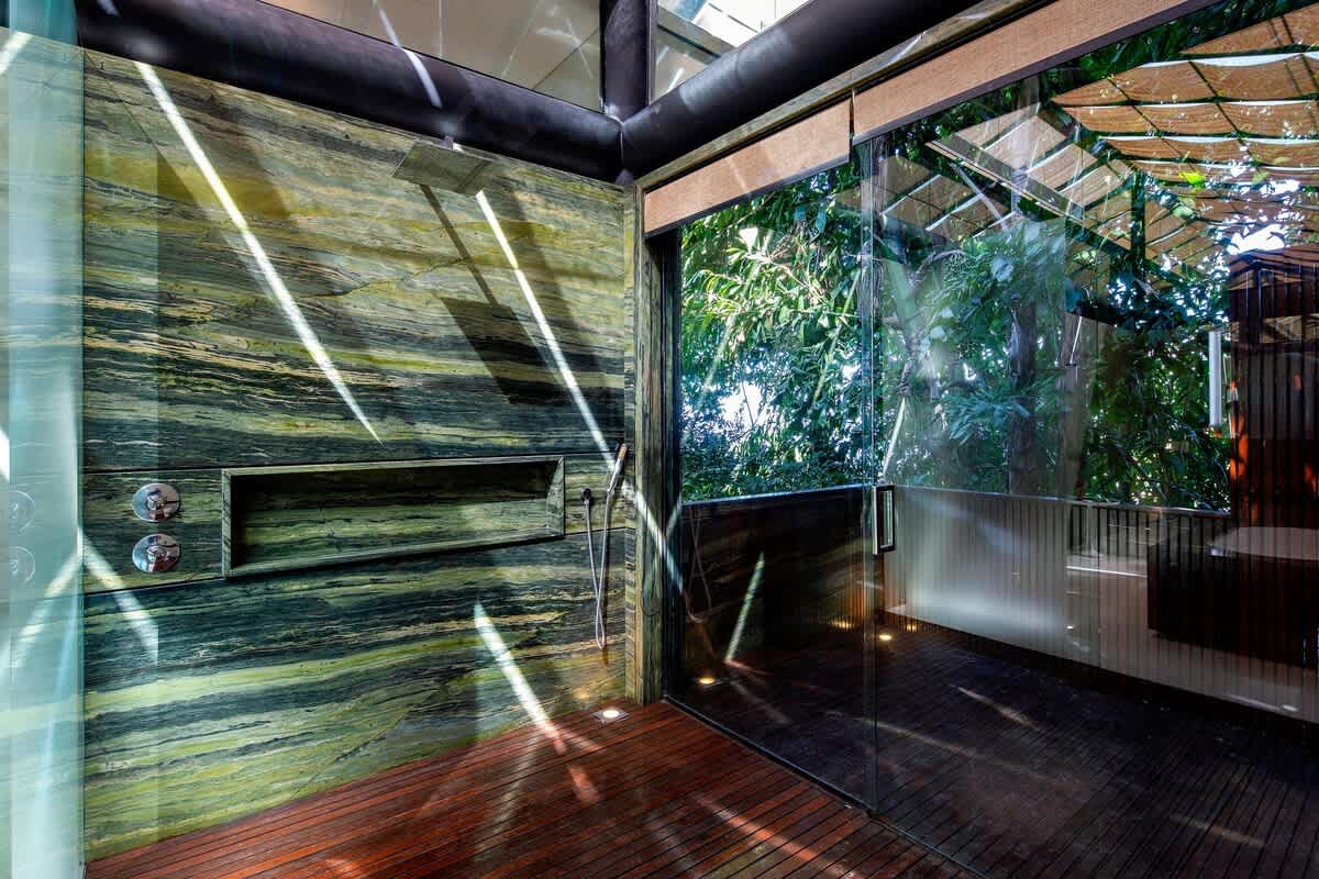 Outdoor shower walled in slab-cut green marble, jungle beyond the glass.